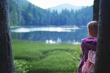 Young caucasian woman hugging a tree in the forest near the lake in summer evening.