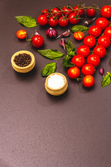 Ripe cherry tomatoes, garlic, basil, salt and black peppercorns on a black stone culinary background