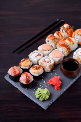 Sushi rolls assortment, wasabi, marinated ginger and soy sauce served on slate plate on black table