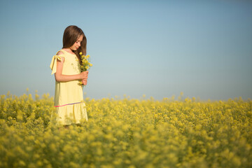 teenage girl in a yellow dress picks flowers in a yellow field in summer