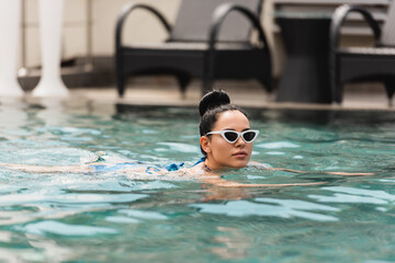 attractive young woman in sunglasses swimming in pool
