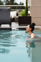 side view of attractive girl in sunglasses swimming in pool