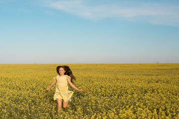 portrait of a teenage girl in a yellow dress running across the field in summer