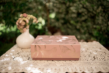 Rosa Box mit Ornamenten auf einem Tisch mit Häkeldecke und Blumenvase