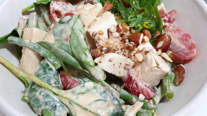 Vegetable salad bowl with white dressing, nuts and seaweed salad, close up view