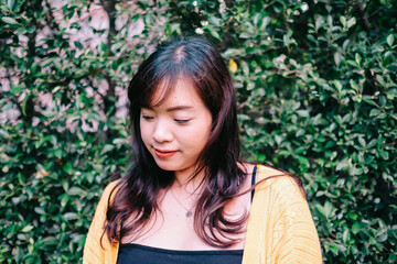 Naklejka premium Close up of young pretty Asian woman in blue yellow sweater with garden background.