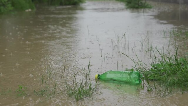An empty plastic bottle of carbonated drinks floats on the water during a flood. Very dirty water, plastic bottles float on the water. It rains and the water level rises.