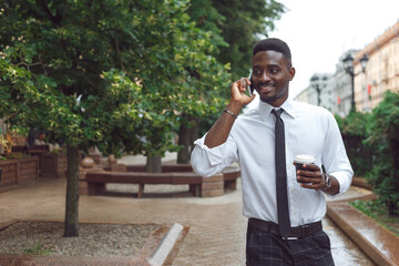 Portrait of happy young african business man speaking on the phone and walking on the street with...