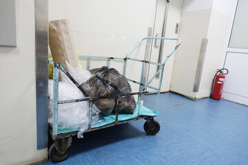 Old metal cart with black garbage bags in poor hospital hole. Dirty wall and blue floor as...