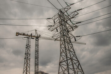 Construction crane working between high voltage electrical transmission towers and lines with dark cloudy sky nobody