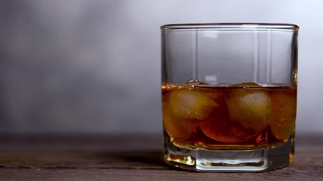 Throws ice and Whiskey poured into a glass with ice on a gray wooden table background. slow motion shot. front view on