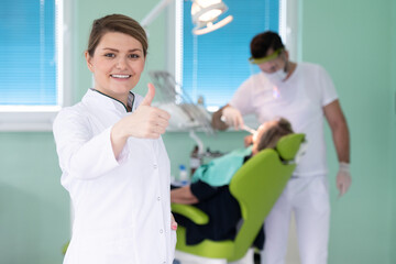 people, medicine, stomatology and healthcare concept - happy young female dentist with tools over medical office background