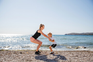 Fototapeta na wymiar A young blonde mother and her blonde son play sports on the rocky sea coast in the summer