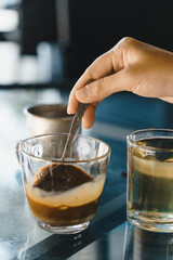 close-up hands of a woman stirring coffee, Hot milk coffee dripping in Vietnam style, pouring water over ground coffee contained in Vietnamese Phin Filter on table. Selective Focus.