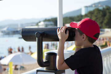 .The boy looks through a telescope located on the embankment at the sea. Children's interest in...