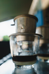 Hot milk coffee dripping in Vietnam style, pouring water over ground coffee contained in Vietnamese Phin Filter on table. Selective Focus.