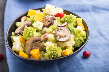 Vegetarian salad from romanesco cabbage, champignons, cranberry, avocado and pumpkin on a black concrete background. side view, selective focus.