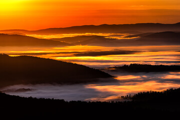 Fototapeta na wymiar A hazy sunrise in the mountains. Mountains silhouettes and fog in the valleys. Photo from Polonina Wetlinska. Bieszczady National Park. Carpathians. Poland.