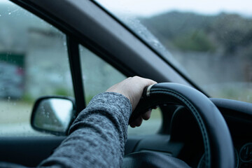 Mano en volante de dirección, conducción con lluvia.