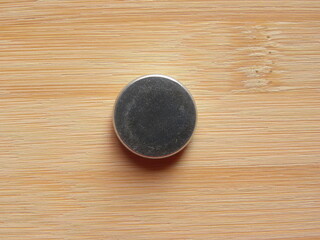 Back side of small silver color round internal magnet of over the ear headphone kept on wooden table