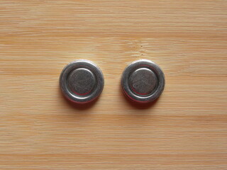 Front side of 2 small silver color round internal magnets of over the ear headphones kept on wooden table