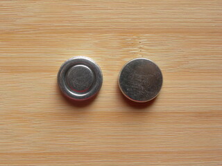 Front and back side of small silver round internal magnet of over the ear headphone kept on wooden...