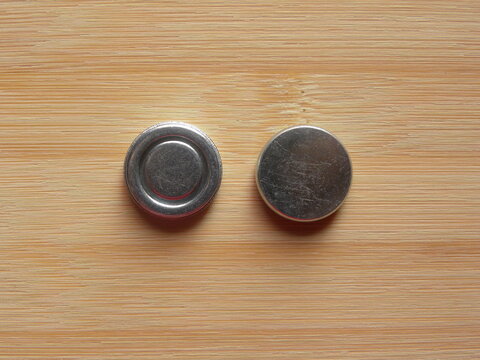 Front and back side of small silver round internal magnet of over the ear headphone kept on wooden table