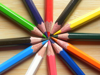 Many color pencils arranged in circle kept on wooden table