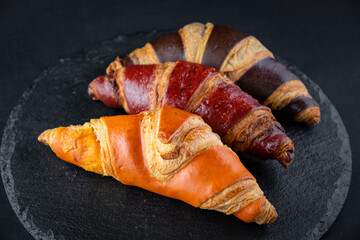 Board with tasty croissants on dark wooden table, closeup. French pastry