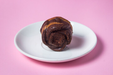 Cupcake on a pink background. A striped cupcake on a white saucer stands on a pink surface