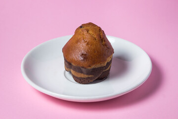 Cupcake on a pink background. A striped cupcake on a white saucer stands on a pink surface