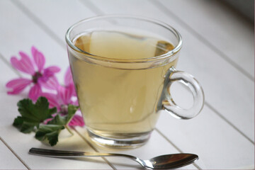 mauve tisane with flowers in vibrant colour and leaves on white wooden table