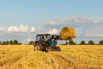 A tractor in field lifts up a hay bale.