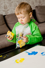 Very serious face. Toddler painting with sponge and hands.