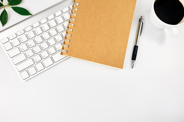 White office desk table. Workspace with keyboard, notebook, office supplies, pen, green leaf, and coffee cup on white background. Top view with copy space, flat lay.