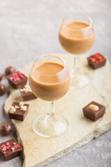 Sweet chocolate liqueur in glass on a gray concrete background and stone slate board. Side view, selective focus.