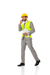 Smiling engineer in hardhat and suit talking on smartphone and holding laptop on white background
