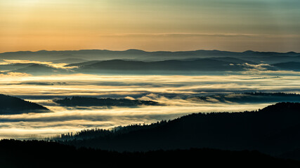 A hazy sunrise in the mountains. Mountains silhouettes and fog in the valleys. Photo from Polonina Wetlinska. Bieszczady National Park. Carpathians. Poland.