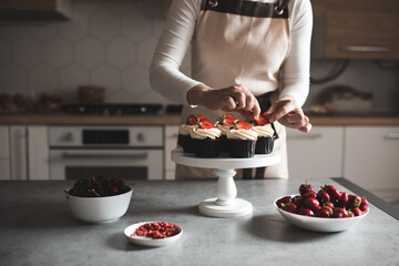 Young woman decorate cupcakes with fruits and cream cheese closeup in kitchen. Working at home....