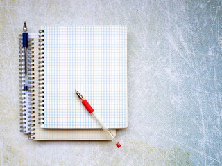 Three notebooks are on top of each other. There is a red pen diagonally on a blank sheet of paper. There is a blue pen on the side of the notebook. Blank space for text in notebook and on background.