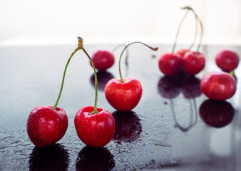 Red cherries, wet with water, are reflected against a black mirror background.