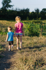 boy and a girl holding hands walking in the field, brother and sister