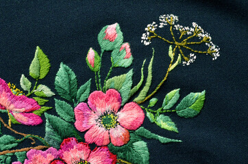 Beautiful pink flowers embroidered on dark fabric. Ukrainian folk embroidery. Fabric decor.