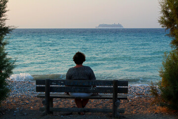 Naklejka na ściany i meble Elderly woman sitting on bench near the sea