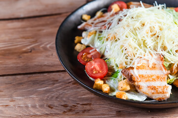 Appetizing Caesar salad with chicken in a black plate on a wooden table. The concept of healthy food and serving