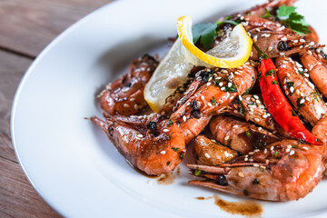 Appetizing fried shrimp with specialties, sesame seeds and lemon, on a white plate on a background of wood. Food concept in restaurants and bars