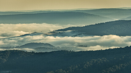A hazy sunrise in the mountains. Mountains silhouettes and fog in the valleys. Photo from Polonina Wetlinska. Bieszczady National Park. Carpathians. Poland.