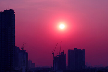 Fototapeta na wymiar Pop art style purple pink colored sky with dazzling sun rising over the silhouette of construction site 