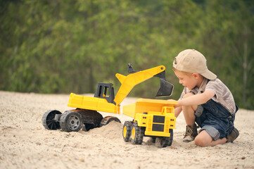 Child, little boy have fun with toy excavator and dumper in the sand. Carefree childhood.