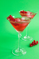 Cold cocktail with red currants in the two martini glasses on the green  background. Location vertical. Closeup.